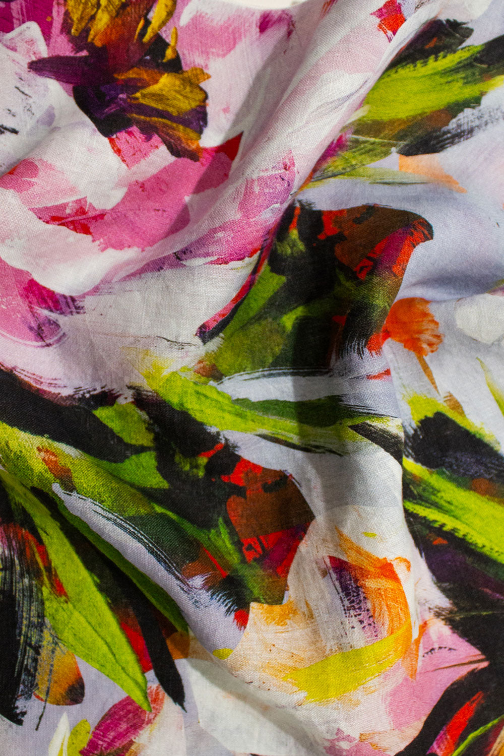 A close-up of a lightweight linen fabric with an abstract floral print, featuring oversized large scale white, pink, green, yellow, and black brushstrokes. @carolynquan.art
